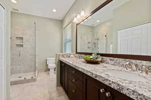 Bathroom featuring toilet, double sink vanity, walk in shower, and tile patterned flooring