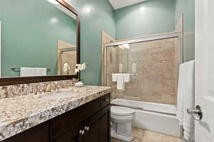 Full bathroom with combined bath / shower with glass door, tile patterned floors, toilet, and vanity