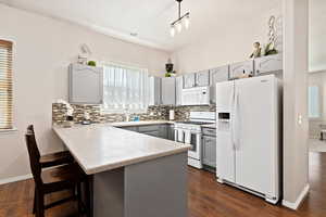 Kitchen featuring a kitchen bar, white appliances, kitchen peninsula, decorative backsplash, and dark hardwood / wood-style floors