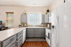 Kitchen with backsplash, dark hardwood / wood-style flooring, white appliances, and gray cabinetry