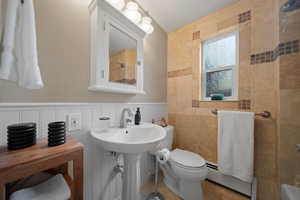 Darling bathroom with a new sink and faucet, toilet, bath and shower combo, baseboard heating, travertine tile, and window