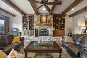 Living room featuring beam ceiling, built in shelves, ceiling fan, a stone fireplace, and wood-type flooring