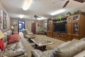 Living room with a textured ceiling, ceiling fan, and carpet flooring