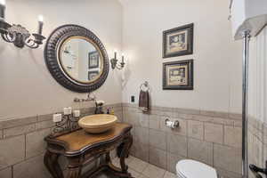 Bathroom with tile walls, tile patterned floors, toilet, and vanity