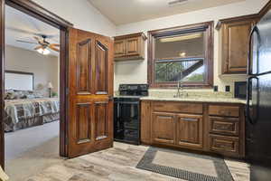 Kitchen with ceiling fan, black appliances, light stone countertops, light carpet, and vaulted ceiling