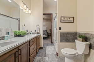 Bathroom with tile patterned flooring, tile walls, double vanity, and toilet