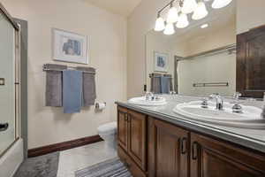 Full bathroom featuring tile patterned floors, double sink vanity, toilet, and enclosed tub / shower combo