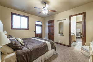 Carpeted bedroom featuring connected bathroom, multiple windows, and ceiling fan