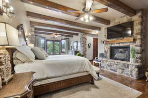 Bedroom featuring a stone fireplace, beamed ceiling, ceiling fan, and hardwood / wood-style floors