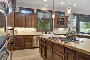 Kitchen with stainless steel appliances, wood counters, sink, hanging light fixtures, and decorative backsplash