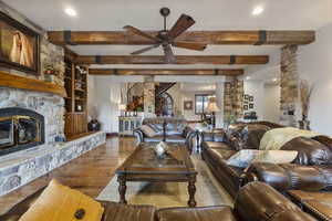 Living room featuring beamed ceiling, hardwood / wood-style flooring, a stone fireplace, built in shelves, and ceiling fan