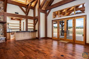 Unfurnished living room with a skylight, french doors, dark wood-type flooring, beamed ceiling, and high vaulted ceiling