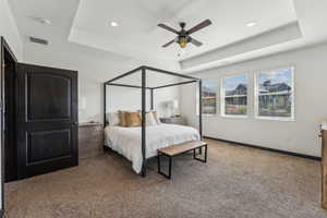 Carpeted bedroom featuring ceiling fan and a tray ceiling