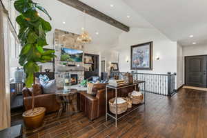 Living room with lofted ceiling with beams, a fireplace, dark wood-type flooring, and an inviting chandelier