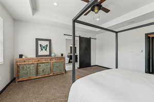 Carpeted bedroom with a tray ceiling, a barn door, and ceiling fan