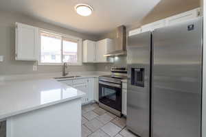 Kitchen featuring white cabinetry, stainless steel appliances, sink, and wall chimney range hood