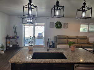 Kitchen with dishwasher, dark hardwood / wood-style floors, light stone counters, and sink