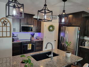 Kitchen featuring dark brown cabinets, sink, granite counters, appliances with stainless steel finishes, and a textured ceiling