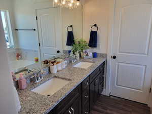 Bathroom with dual vanity, wood-type flooring,  two shower heads in a separate shower, and a bathing tub