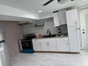 Kitchen featuring electric stove, white cabinets, sink, fridge, and dark stone countertops