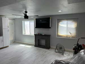 Unfurnished living room with a textured ceiling, light wood-type flooring, and ceiling fan