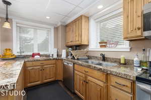 Lower Level Kitchen with stainless steel appliances, hanging light fixtures, ornamental molding, sink, and light stone countertops