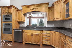 Kitchen with dark stone counters, appliances with stainless steel finishes, tasteful backsplash, and sink