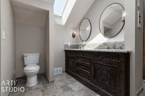 Primary bathroom with tasteful backsplash, a skylight, dual vanity, toilet, and tile patterned flooring