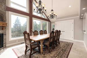 Tiled dining area featuring a stone fireplace, a towering ceiling, and a chandelier