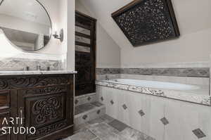 Primary bathroom with tile patterned floors, vaulted ceiling, vanity, and a bathtub