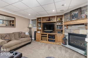 Lower Level Living room featuring a drop ceiling, built in features, ornamental molding, carpet floors, and a stone fireplace