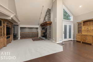 Lving room with track lighting, a stone fireplace, french doors, high vaulted ceiling, and wood-type flooring