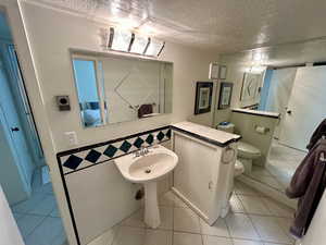 Bathroom with tile patterned floors, toilet, sink, and a textured ceiling