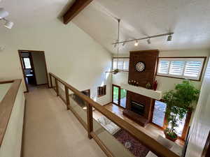 Hall with vaulted ceiling with beams, light hardwood / wood-style flooring, rail lighting, a textured ceiling, and brick wall