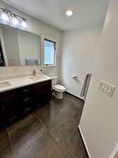 Bathroom featuring tile patterned flooring, dual vanity, toilet, and a textured ceiling