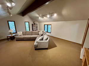 Carpeted living room with a textured ceiling, vaulted ceiling with beams, and track lighting