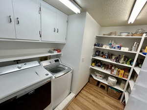 Clothes washing area with cabinets, washer and clothes dryer, light wood-type flooring, and a textured ceiling