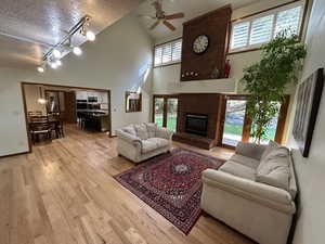 Living room featuring rail lighting, light wood-type flooring, a textured ceiling, a brick fireplace, and brick wall