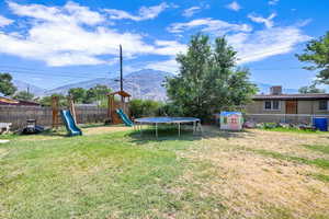 View of yard with a mountain view, a trampoline, a playground, and a shed