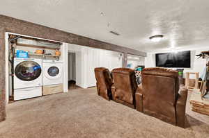 Carpeted home theater room featuring washer and clothes dryer and a textured ceiling