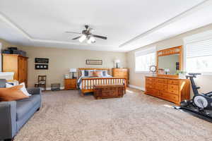 Bedroom with light carpet, ceiling fan, and a tray ceiling