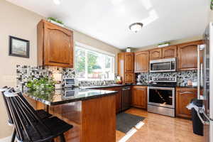 Kitchen with appliances with stainless steel finishes, light hardwood / wood-style flooring, tasteful backsplash, a breakfast bar, and kitchen peninsula