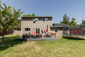 Rear view of property with a trampoline, a deck, and a yard