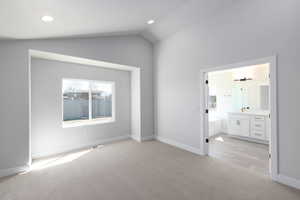 Unfurnished bedroom featuring lofted ceiling, light carpet, and connected bathroom