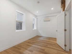 Unfurnished room featuring a wall mounted AC and light wood-type flooring