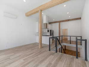 Interior space featuring sink, an AC wall unit, beamed ceiling, and light wood-type flooring