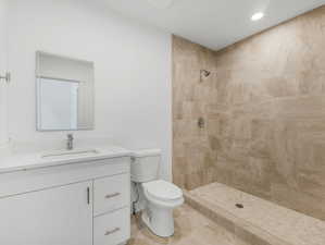 Bathroom with tiled shower, tile patterned flooring, toilet, and vanity