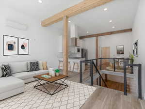 Living room with beam ceiling, sink, a wall unit AC, and light wood-type flooring