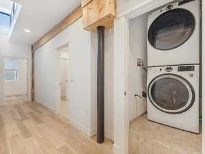 Laundry room with a skylight, light hardwood / wood-style flooring, and stacked washer / drying machine