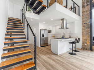 Kitchen featuring wall chimney range hood, a high ceiling, light wood-type flooring, and stainless steel appliances